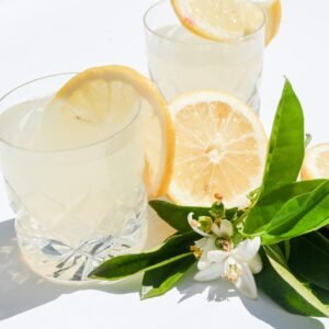 A bright still life of citrus drinks garnished with lemons and white blossoms.