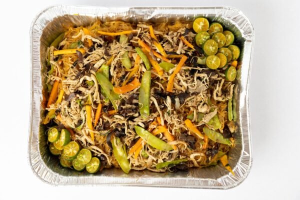 Delicious Pancit Bihon with vegetables and calamansi in an aluminum tray, top view.