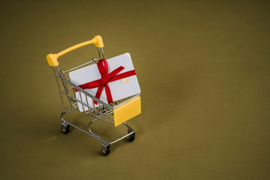 A gift card with a red bow sits in a mini shopping cart on a yellow backdrop.