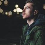 A young man in a jacket gazes thoughtfully upwards, illuminated by city lights.
